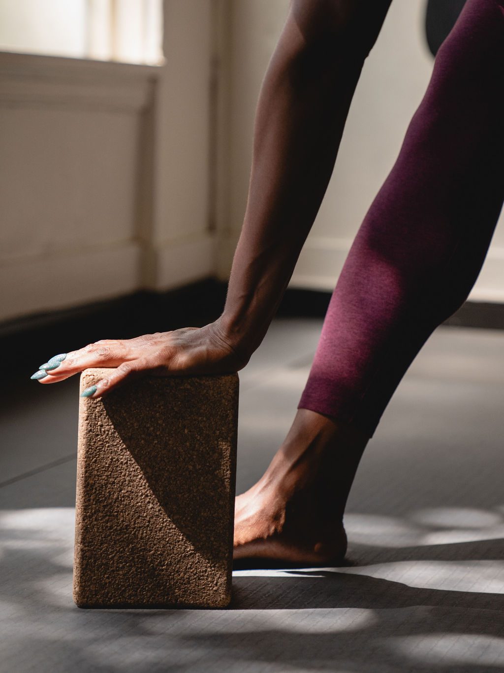 Close-up of Tameka's hand resting on a cork yoga block in dappled light.